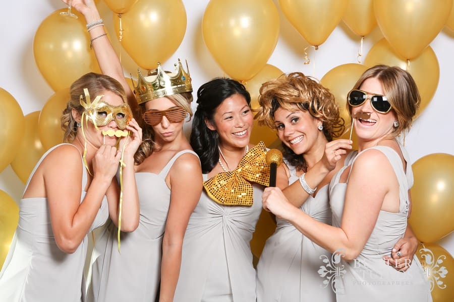 Bridesmaids posing with photo booth props in front of gold balloons